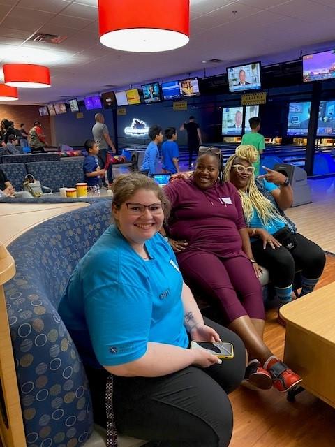 People sitting on a bench in a bowling alley with colorful lights and screens in the background.